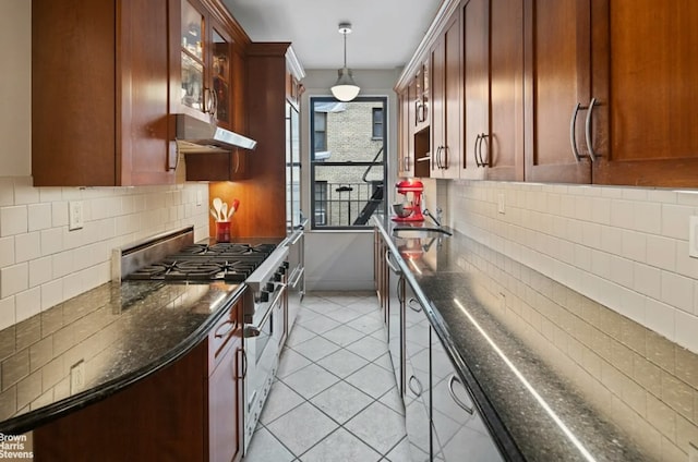 kitchen featuring decorative light fixtures, high end range, glass insert cabinets, dark stone counters, and under cabinet range hood