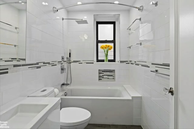 bathroom with tile walls, a sink, bathing tub / shower combination, and toilet