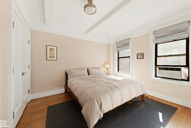 bedroom with beam ceiling, baseboards, and wood finished floors