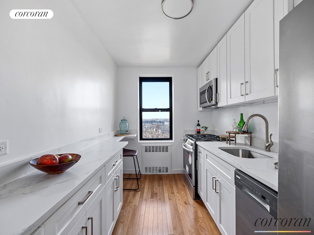 kitchen featuring light wood finished floors, radiator heating unit, appliances with stainless steel finishes, white cabinets, and a sink