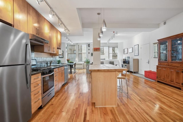 kitchen with a center island, a breakfast bar, stainless steel appliances, dark countertops, and under cabinet range hood