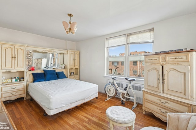 bedroom featuring an inviting chandelier, radiator heating unit, and wood finished floors