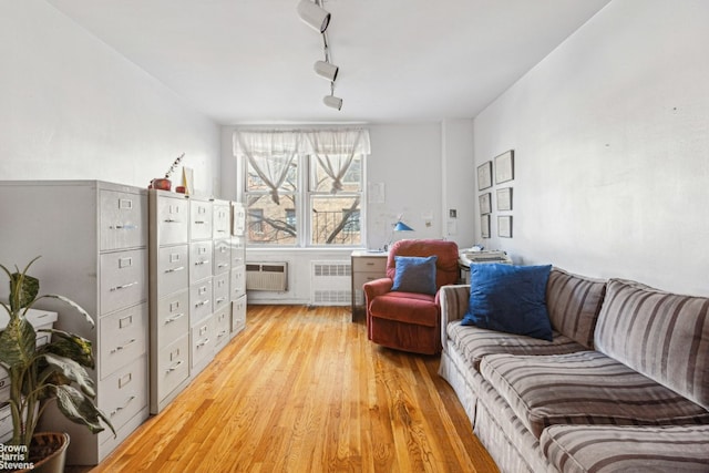 sitting room featuring a wall mounted AC, light wood-type flooring, rail lighting, and radiator