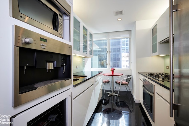 kitchen with glass insert cabinets, dark countertops, white cabinetry, and stainless steel appliances