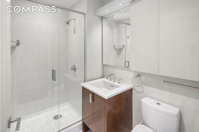 full bath with a stall shower, toilet, vanity, and tile walls