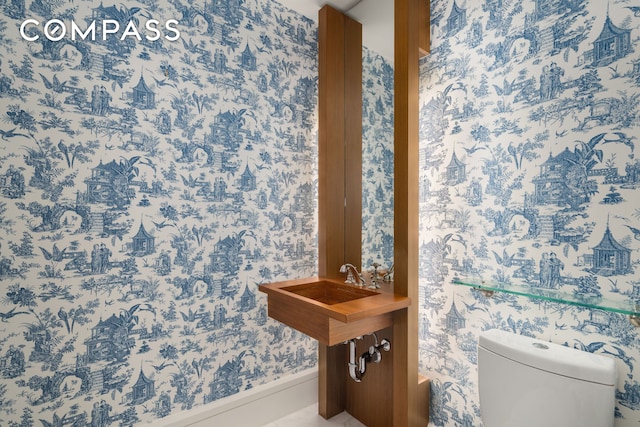 half bathroom with wallpapered walls, toilet, and baseboards