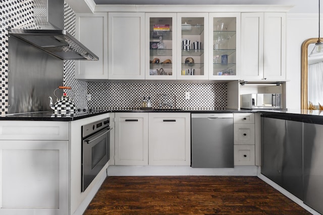 kitchen with dark countertops, stainless steel appliances, wall chimney exhaust hood, and tasteful backsplash