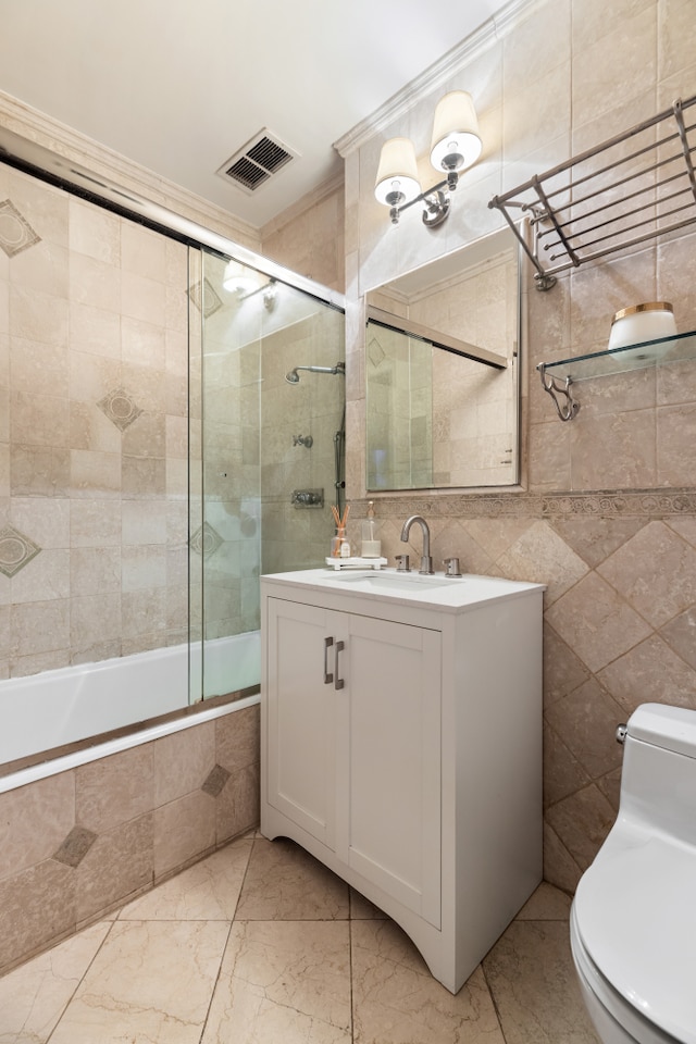 bathroom with visible vents, toilet, tiled shower / bath combo, vanity, and tile walls