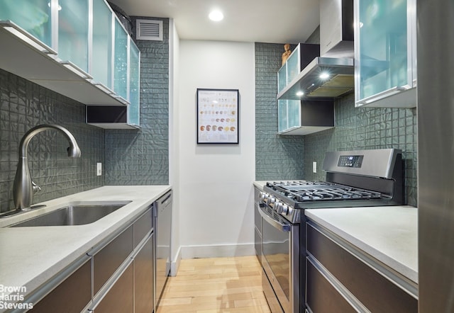 kitchen with stainless steel appliances, visible vents, light countertops, a sink, and wall chimney range hood