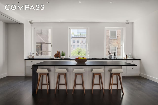 kitchen with dark wood finished floors, a breakfast bar area, dark countertops, and white cabinetry