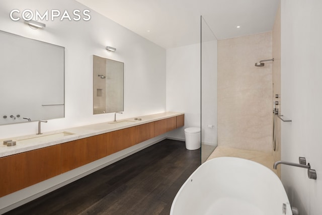 bathroom featuring double vanity, a shower, wood finished floors, a freestanding bath, and a sink