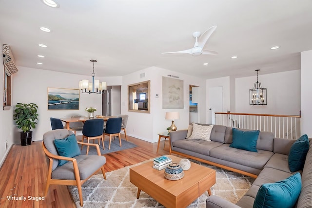 living room with light wood-style flooring, recessed lighting, ceiling fan with notable chandelier, visible vents, and baseboards