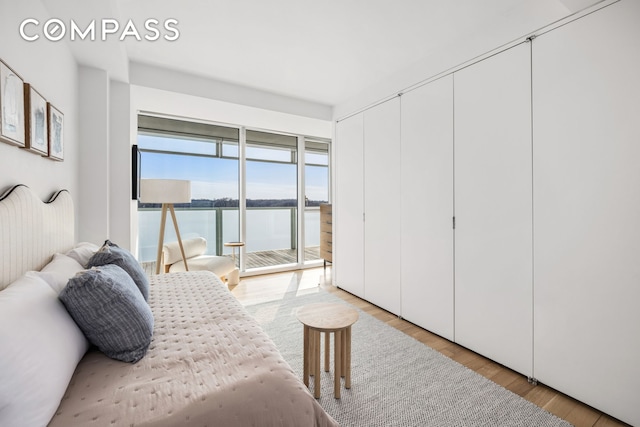 bedroom featuring light wood-type flooring, access to outside, and a water view