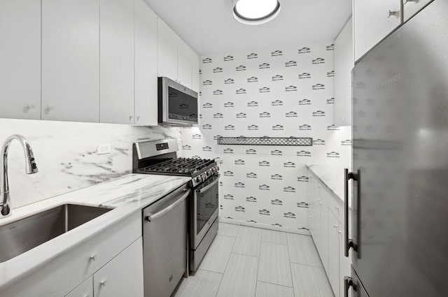 kitchen with wallpapered walls, appliances with stainless steel finishes, white cabinets, and a sink