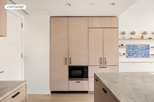 kitchen with black microwave, light brown cabinets, and light stone countertops