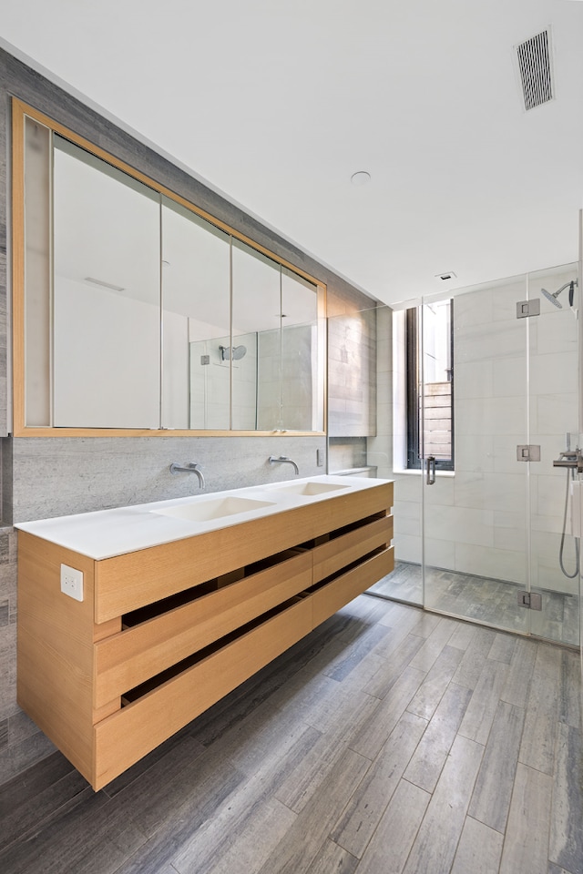 bathroom with double vanity, a shower stall, visible vents, and wood finished floors