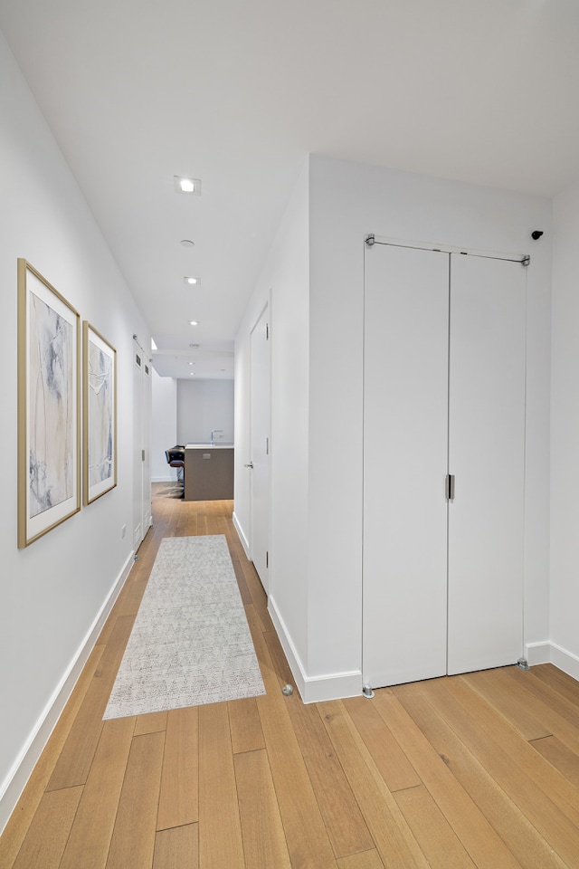 corridor with light wood finished floors, baseboards, and recessed lighting