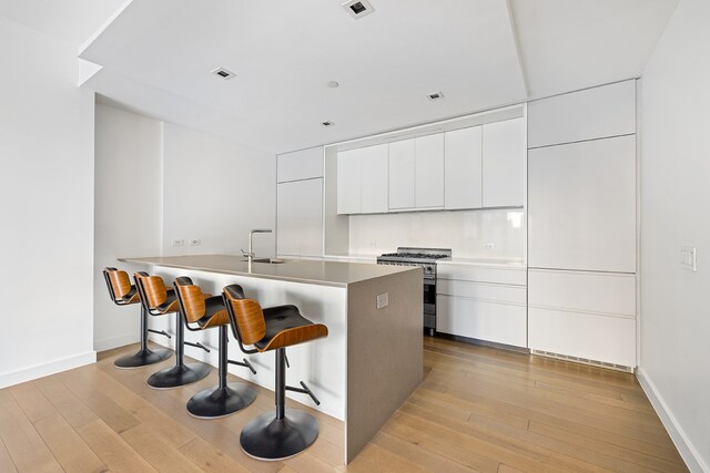 150 Rivington St Unit 2H, New York City, NY 10002 - kitchen with white cabinets, modern cabinets, a sink, stainless steel stove, and a breakfast bar