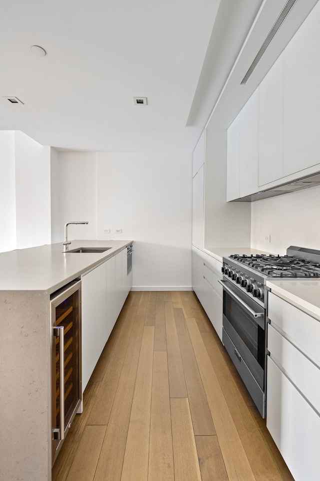 kitchen with a sink, wine cooler, high end stove, and white cabinets