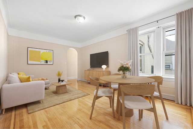 dining space featuring arched walkways, ornamental molding, wood finished floors, and baseboards