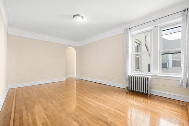 empty room featuring arched walkways, radiator heating unit, plenty of natural light, and a decorative wall