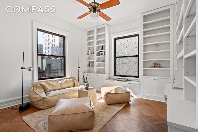 sitting room featuring built in shelves, a ceiling fan, and baseboards