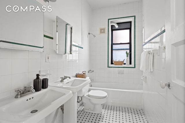 bathroom with toilet, a sink, tile patterned flooring, bathtub / shower combination, and tile walls