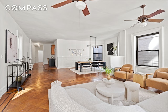 living area with parquet flooring, ceiling fan, and wainscoting