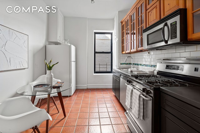 kitchen with light tile patterned floors, stainless steel appliances, tasteful backsplash, brown cabinetry, and glass insert cabinets