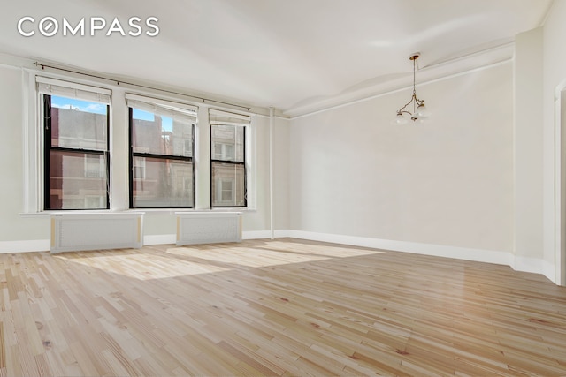 spare room featuring a chandelier, radiator heating unit, light wood-style flooring, and baseboards