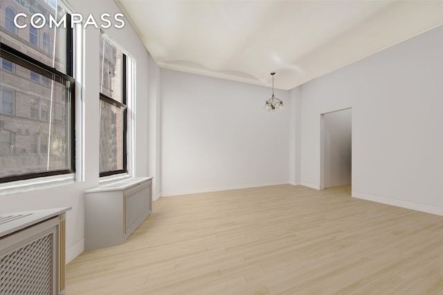 spare room with a healthy amount of sunlight, light wood-type flooring, a chandelier, and baseboards