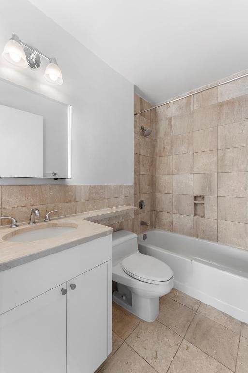 bathroom featuring toilet, tile patterned flooring, vanity, tile walls, and shower / bathing tub combination