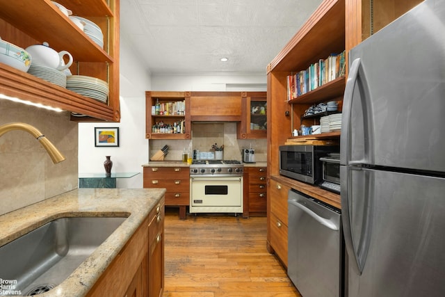 kitchen with open shelves, appliances with stainless steel finishes, a sink, brown cabinetry, and backsplash