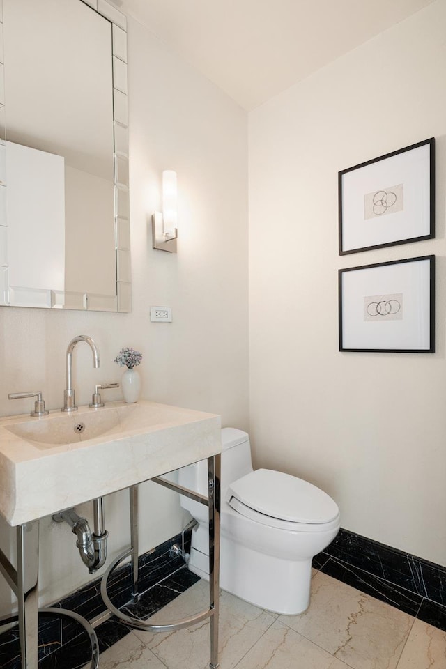 half bathroom with toilet, marble finish floor, and baseboards