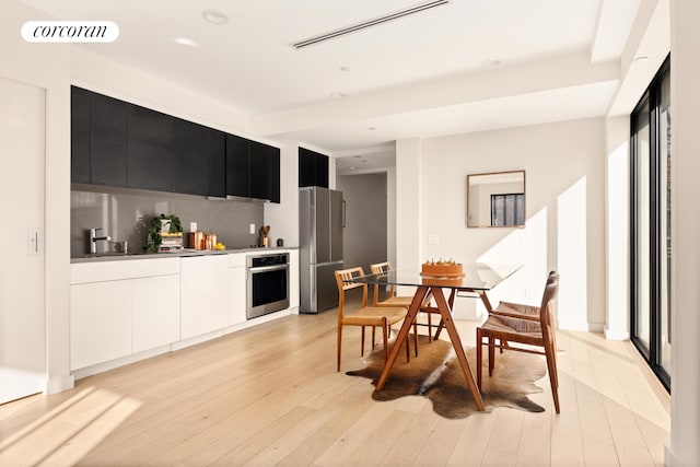 kitchen with appliances with stainless steel finishes, modern cabinets, dark cabinetry, light wood-style flooring, and tasteful backsplash