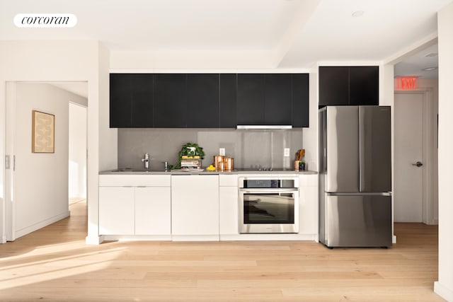 kitchen featuring appliances with stainless steel finishes, dark cabinets, backsplash, light wood finished floors, and white cabinets