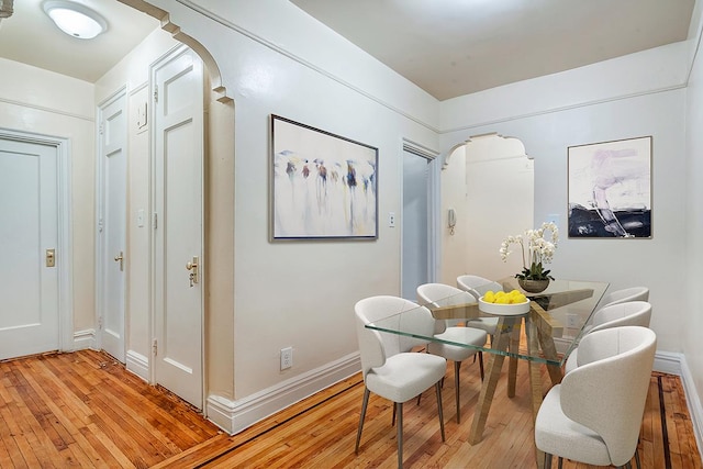 dining room featuring light wood-type flooring, arched walkways, and baseboards