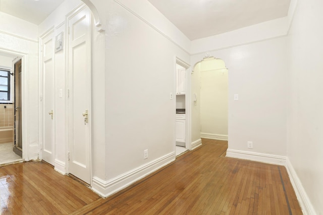 corridor featuring baseboards, arched walkways, and hardwood / wood-style floors