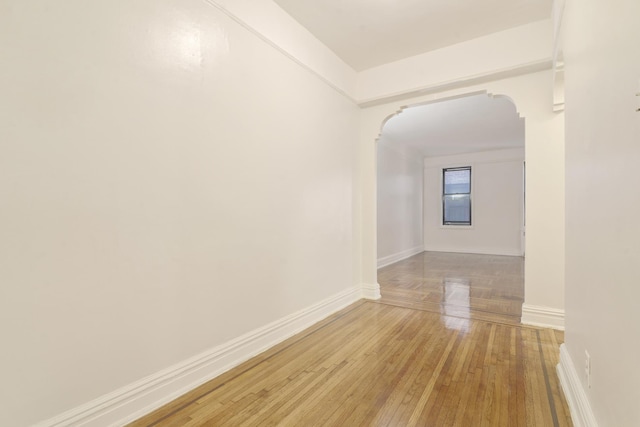 spare room with arched walkways, light wood-style flooring, and baseboards