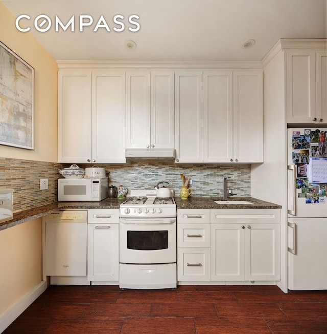 kitchen with under cabinet range hood, white appliances, dark wood-type flooring, a sink, and dark stone counters