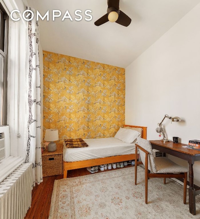 bedroom with an accent wall, dark wood-style flooring, radiator heating unit, and wallpapered walls