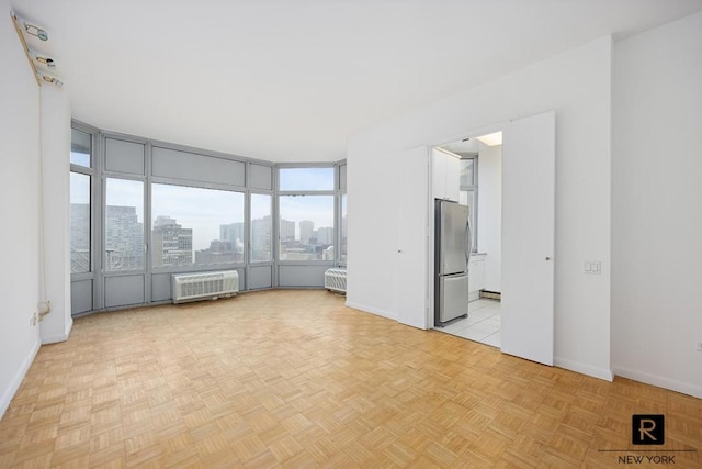 empty room featuring a wall unit AC, a sunroom, a view of city, and baseboards