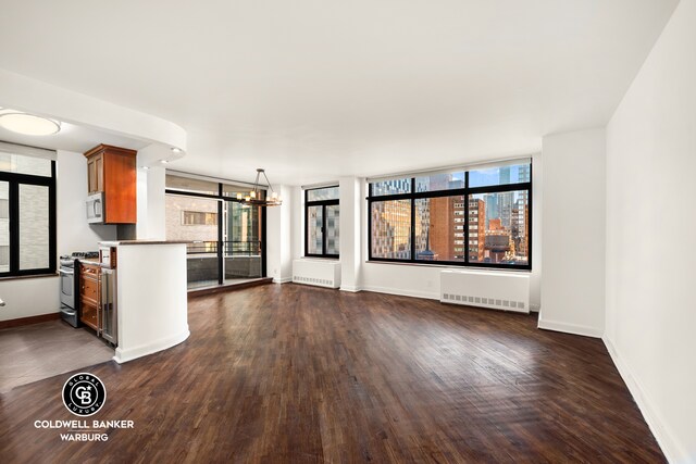 unfurnished living room with dark wood-style flooring, baseboards, a wealth of natural light, and radiator