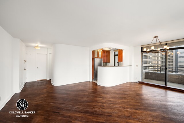 unfurnished living room featuring arched walkways, a chandelier, and dark wood-style floors