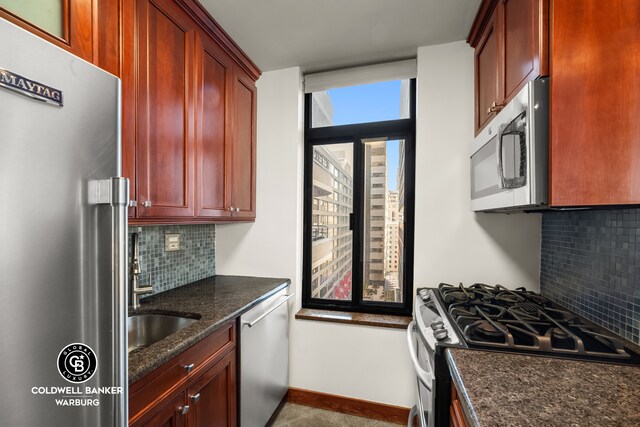 kitchen with dark brown cabinets, dark stone counters, stainless steel appliances, baseboards, and backsplash