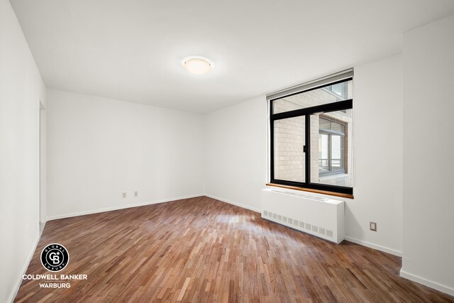 empty room with radiator, baseboards, and wood finished floors