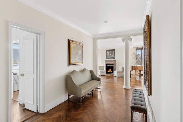 sitting room featuring ornamental molding, baseboards, a lit fireplace, and ornate columns