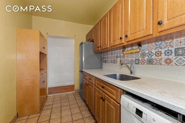 kitchen with light tile patterned floors, white dishwasher, a sink, light countertops, and decorative backsplash