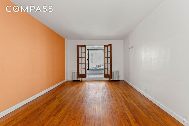 empty room featuring baseboards, wood finished floors, and radiator