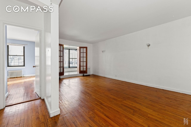 spare room featuring baseboards, radiator heating unit, a wealth of natural light, and hardwood / wood-style flooring